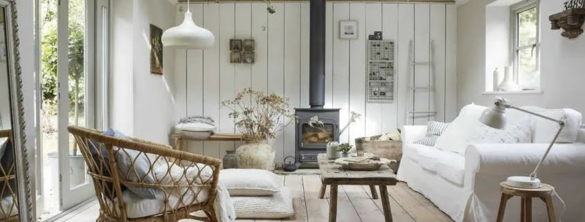 Case arredate in stile provenzale salottino che predilige il colore bianco, tavolino in legno e sedia di vimini. Una stufa a legna scalda la stanza. Sono presenti fiori, piante secche e rampicanti